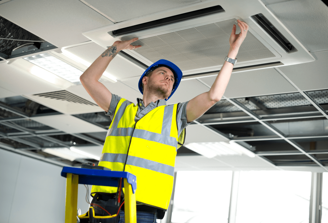 A subcontractor worker fitting an air conditioning unit who has been hired by an all-in-one office fit out specialist that offers comprehensive office renovation services. 